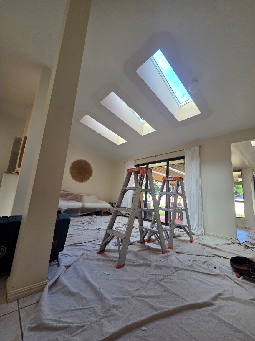 Three new skylights in a living room ceiling, with ladders and drop sheets still in place.