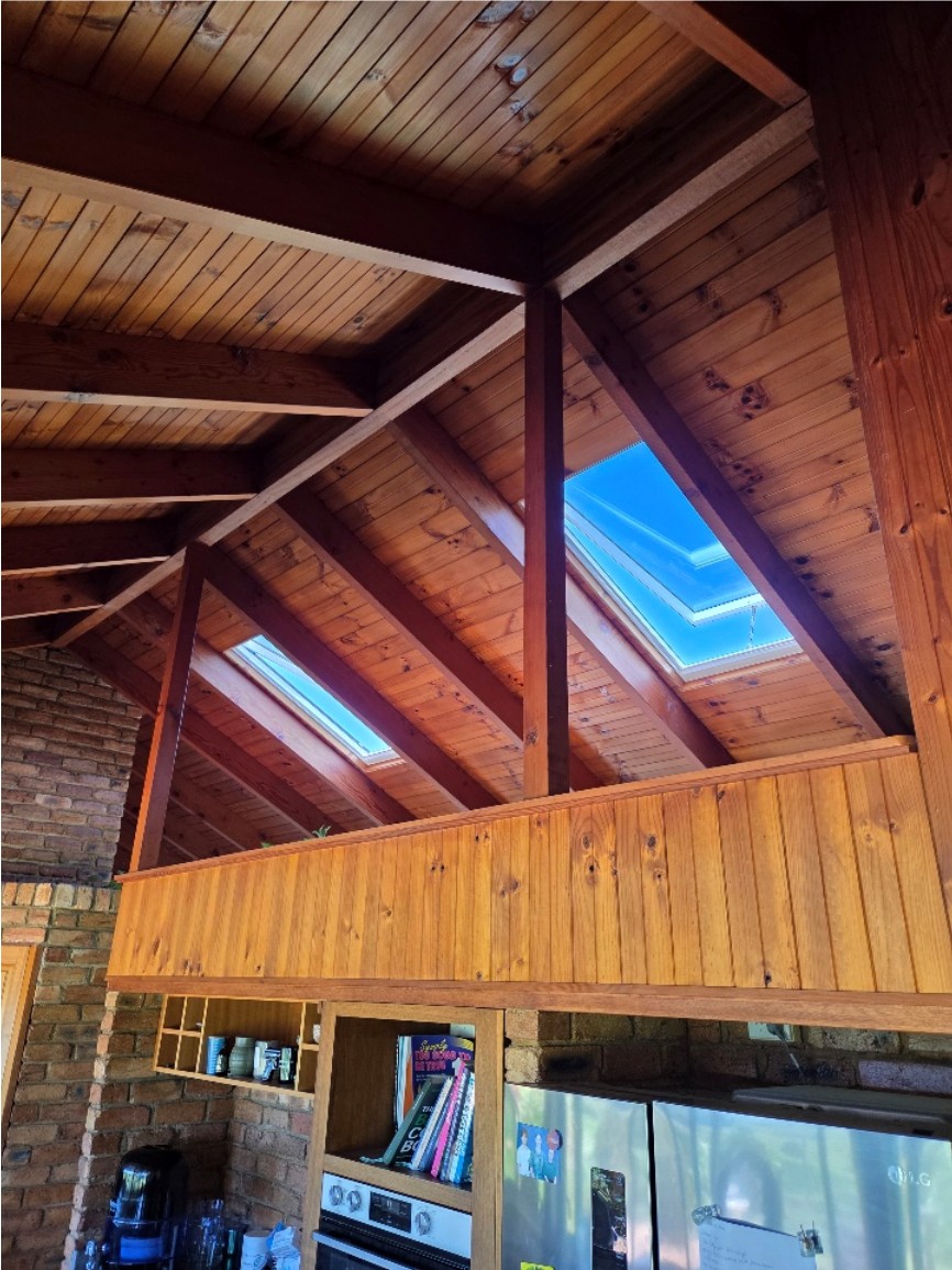 Two skylights set into a timber lined raked ceiling above a kitchen.