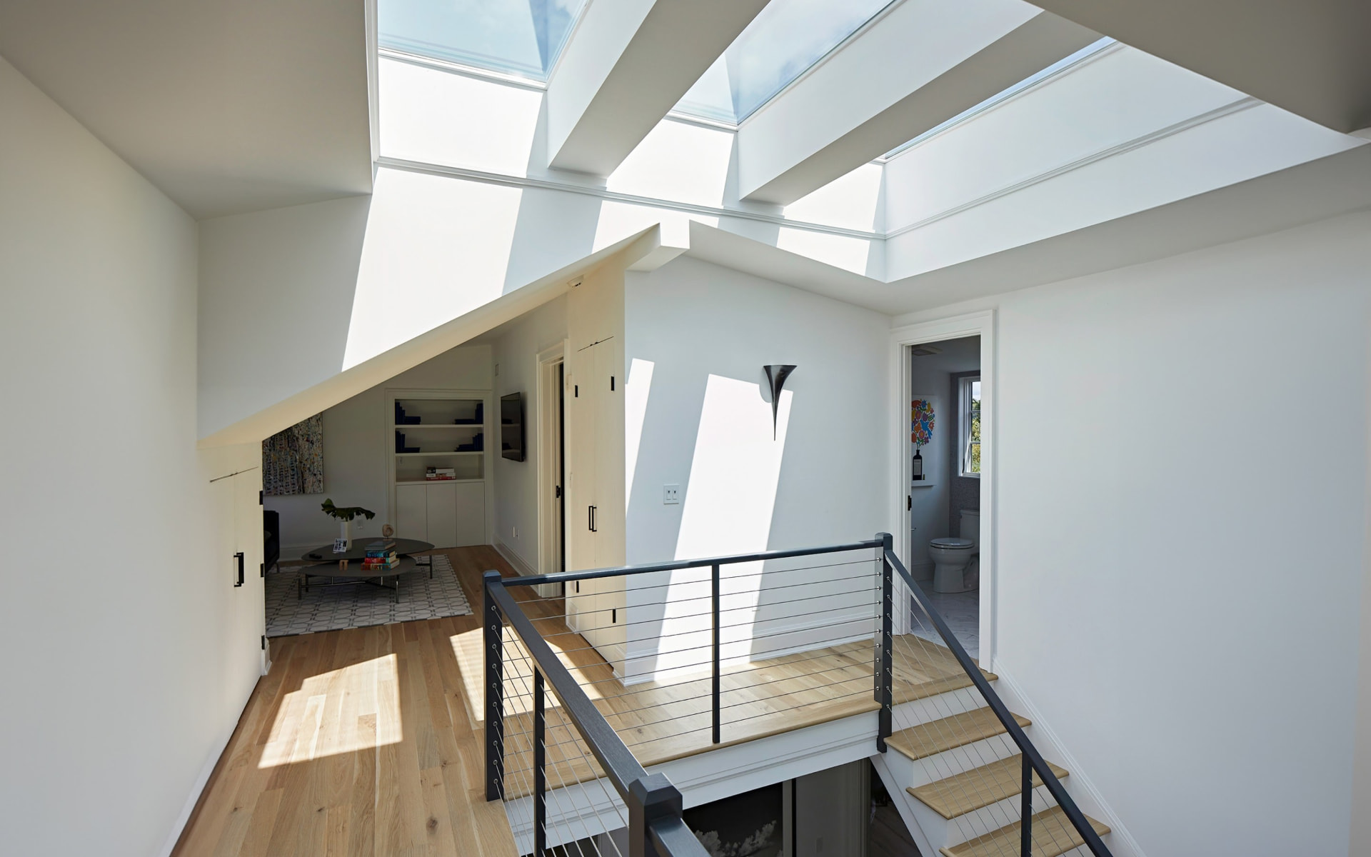 Daylight from a run of ceiling skylights falling across an upper hallway and stair.