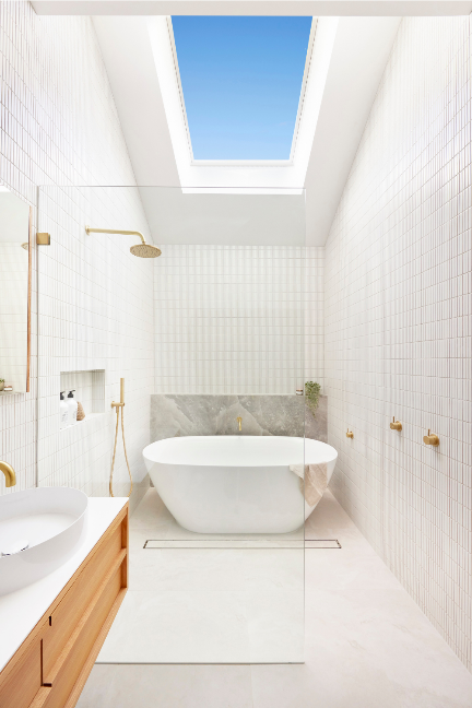 Daylight from a ceiling skylight falling across a bathroom wall and freestanding bath