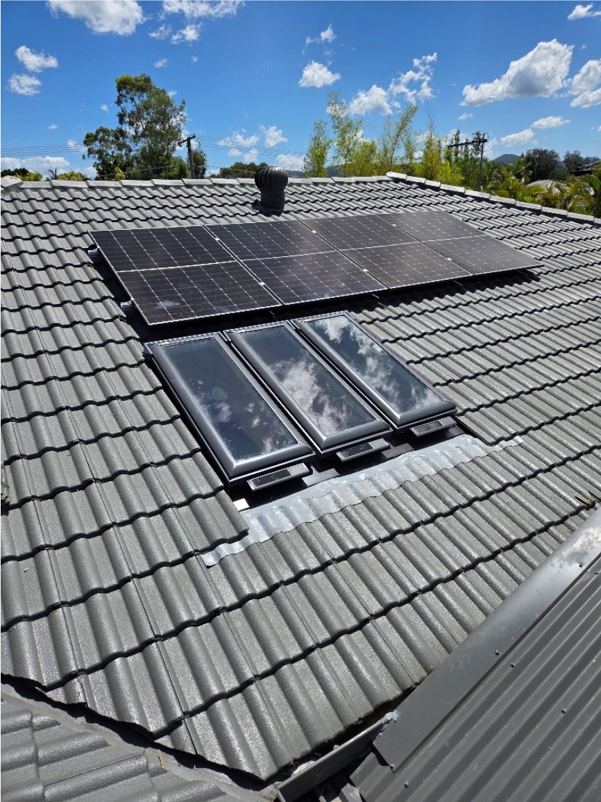 Three skylights installed in a tiled roof beside solar panels.