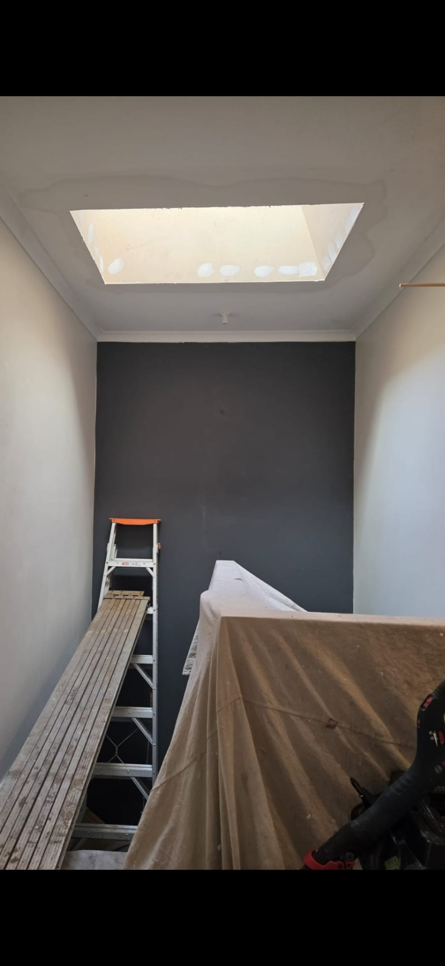A skylight shaft part way through installation, with drop sheets and a work platform in the room below.