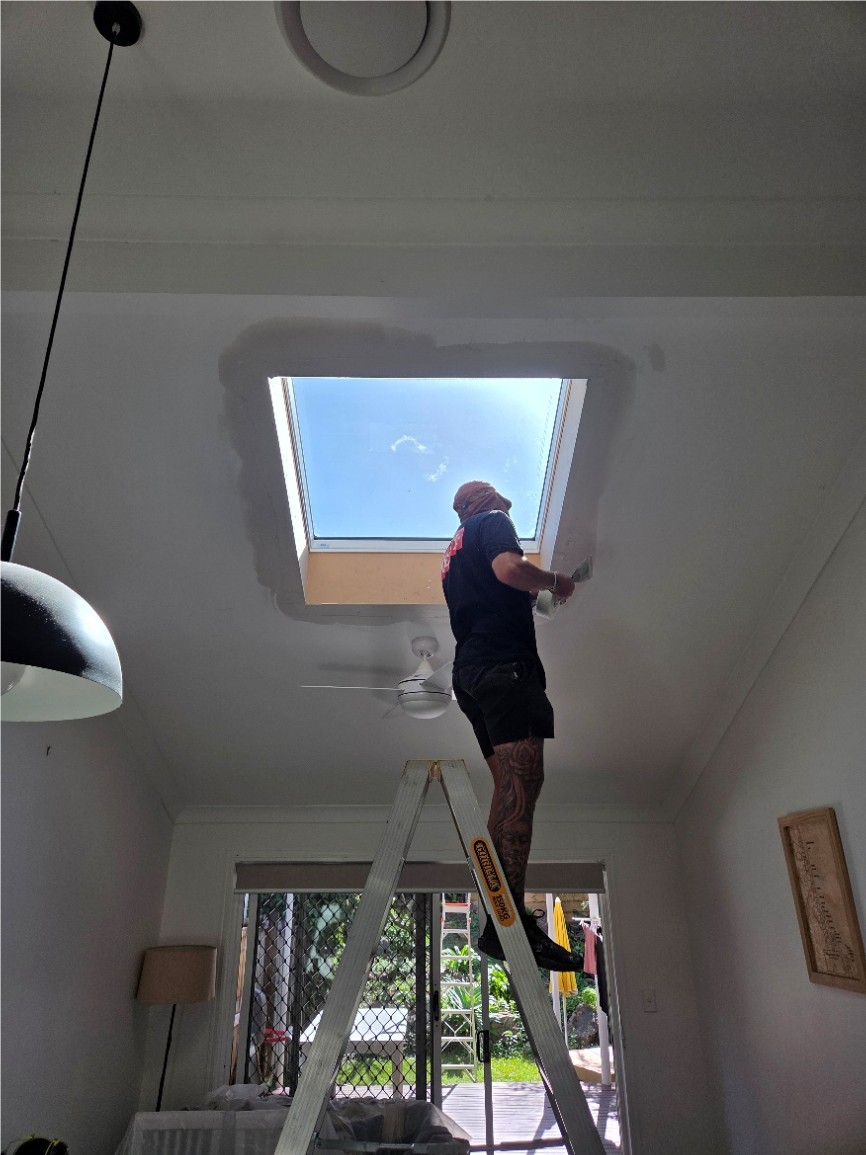 Installer on a ladder working around a new skylight opening in a ceiling.