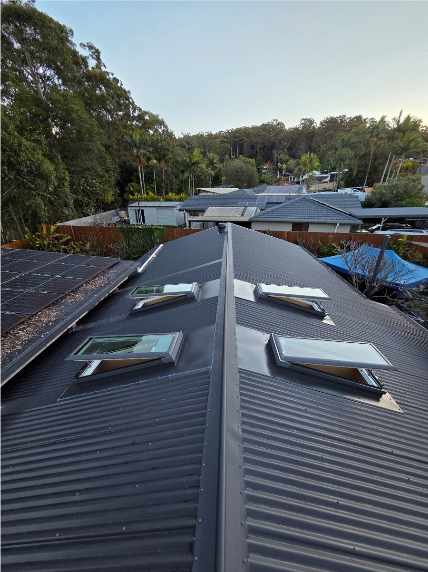 Four skylights installed either side of the ridge on a dark metal roof.