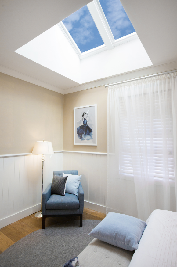 A bedroom with daylight from a ceiling skylight washing down the wall