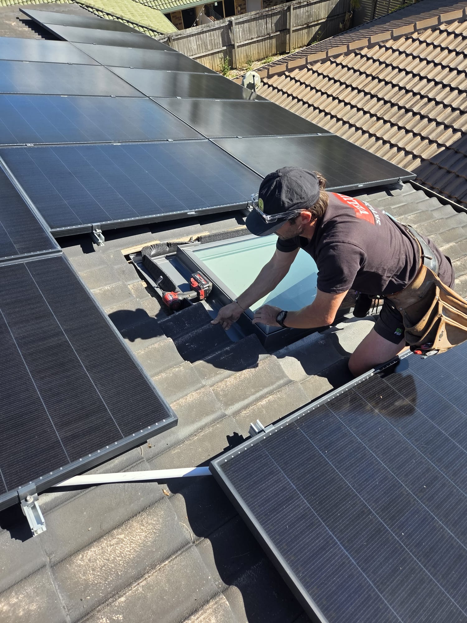 Installer working on a roof skylight beside solar panels.