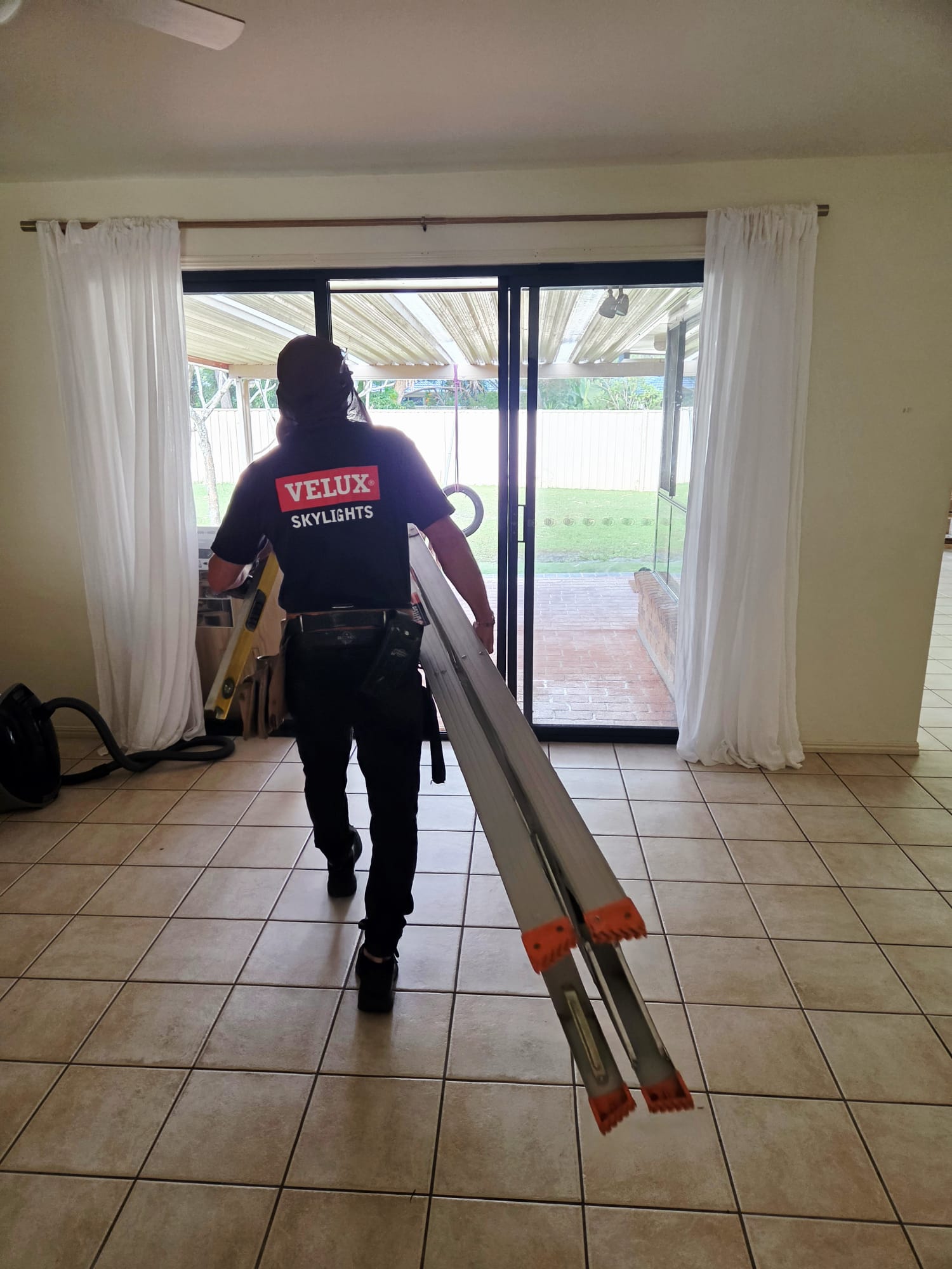 Installer carrying a ladder and tools through a home before a skylight installation.