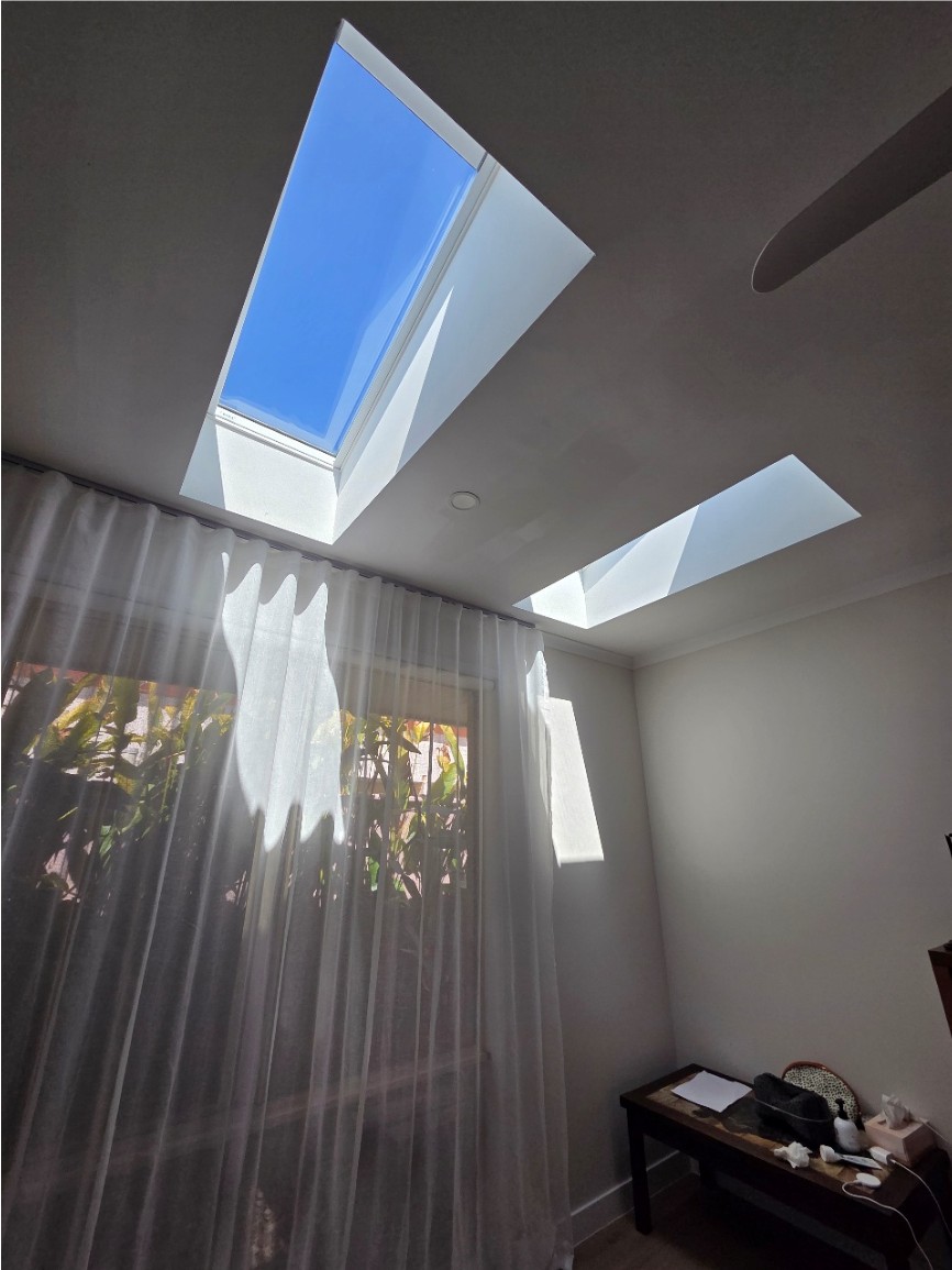 Two skylights in a bedroom ceiling above sheer curtains.