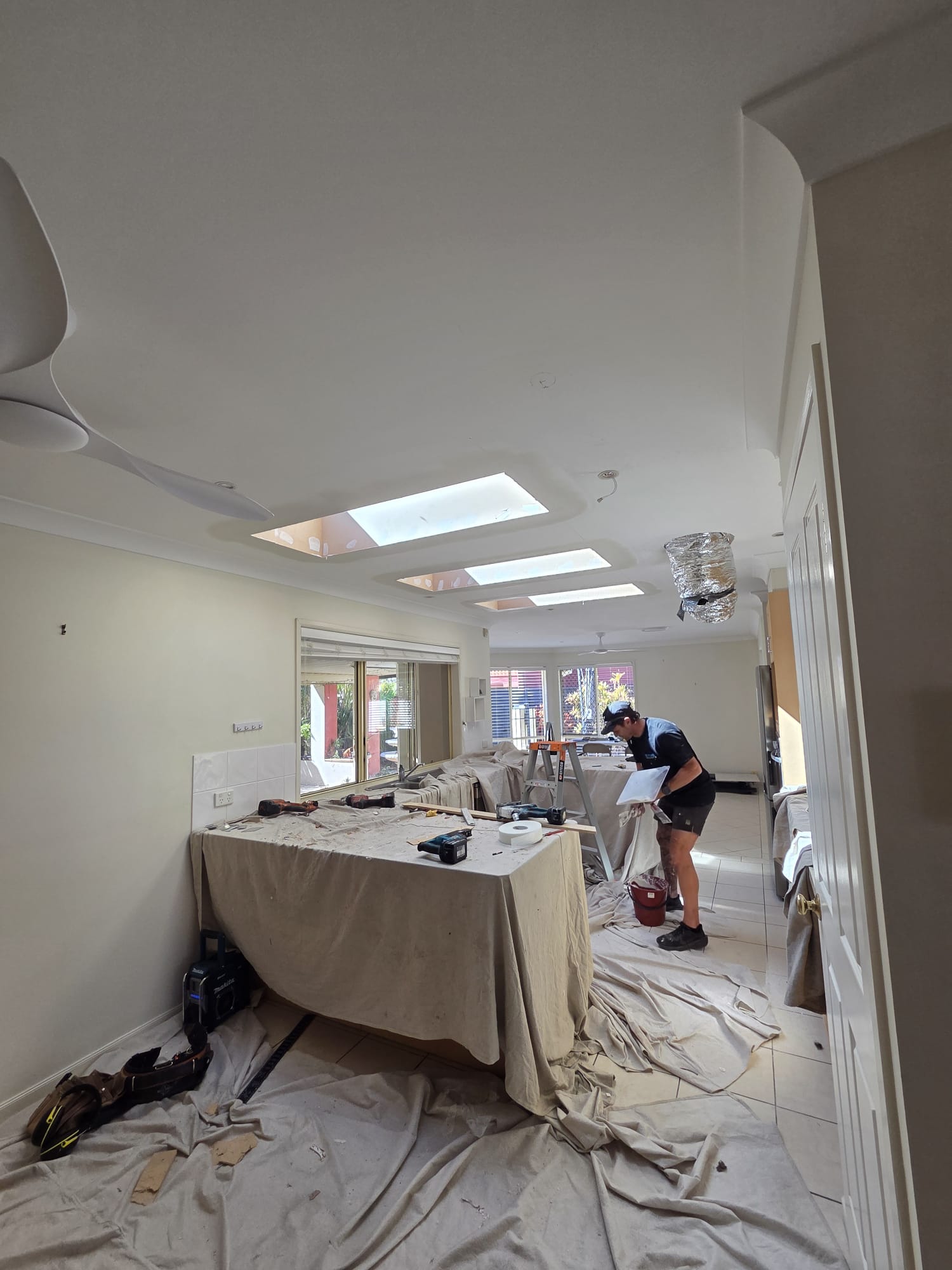Three skylight openings in a row across a plaster ceiling, photographed during installation with the room protected by drop sheets.