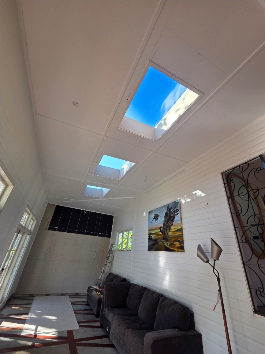 Three skylights in the ceiling of a white lined room with a sofa below.